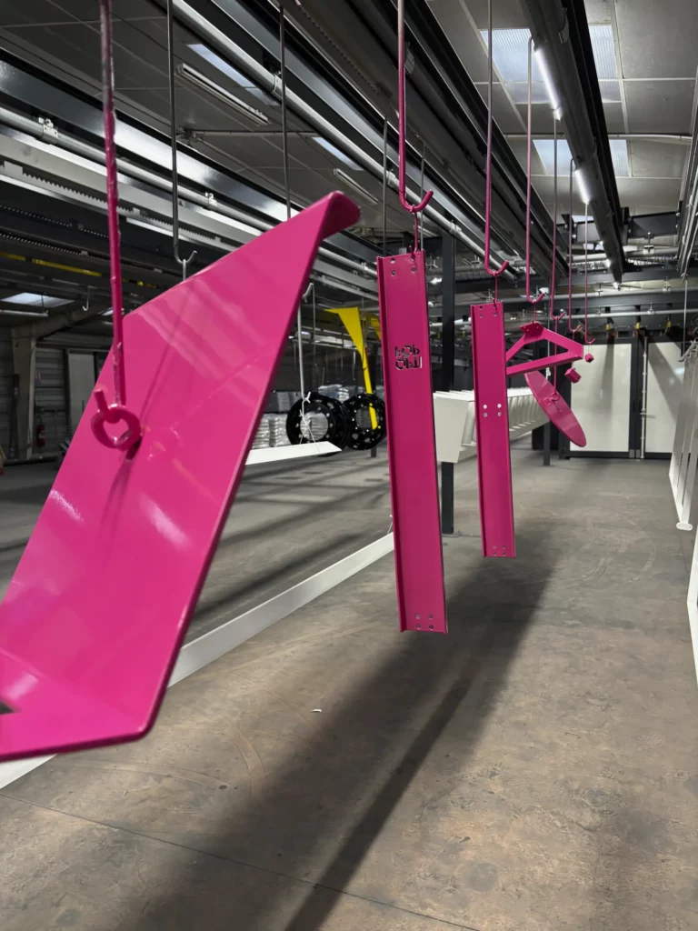Pièces de mobilier métallique laquées rose fuchsia, suspendues avant séchage